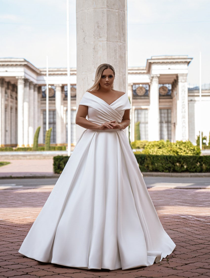 Woman in a white off-shoulder gown standing in front of classical architecture.