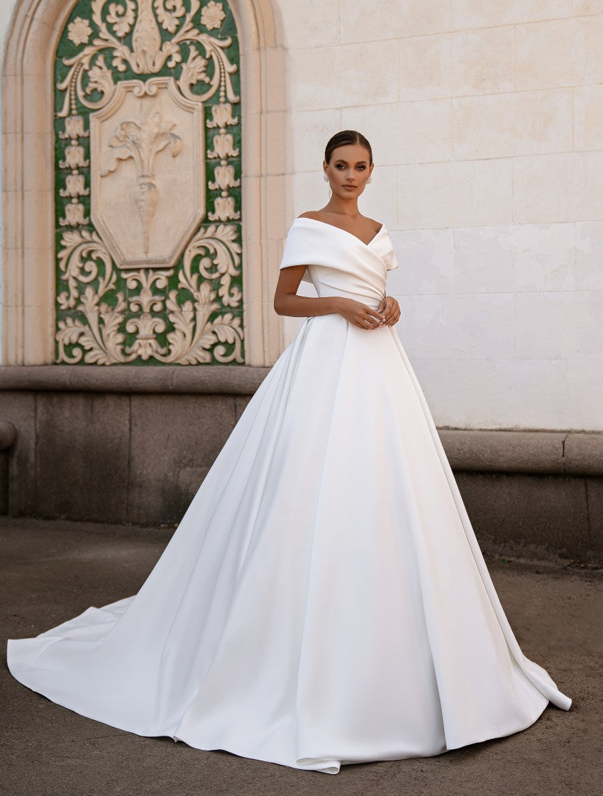 Woman in a white wedding dress standing in front of an ornate wall.