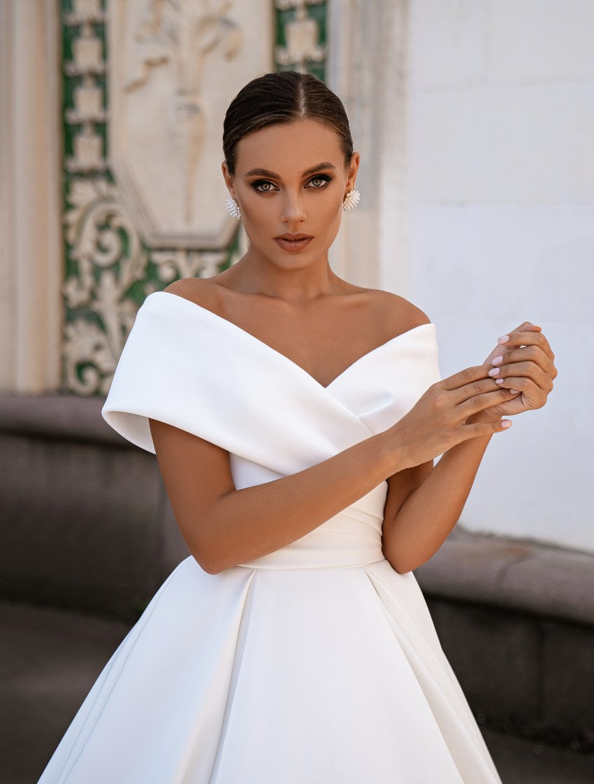 Woman wearing a white off-shoulder dress in an elegant setting.
